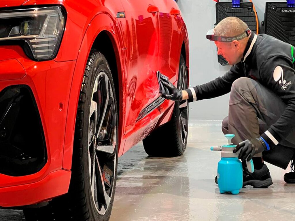 Майстер наносить кварцове покриття на бічну частину червоного Audi.